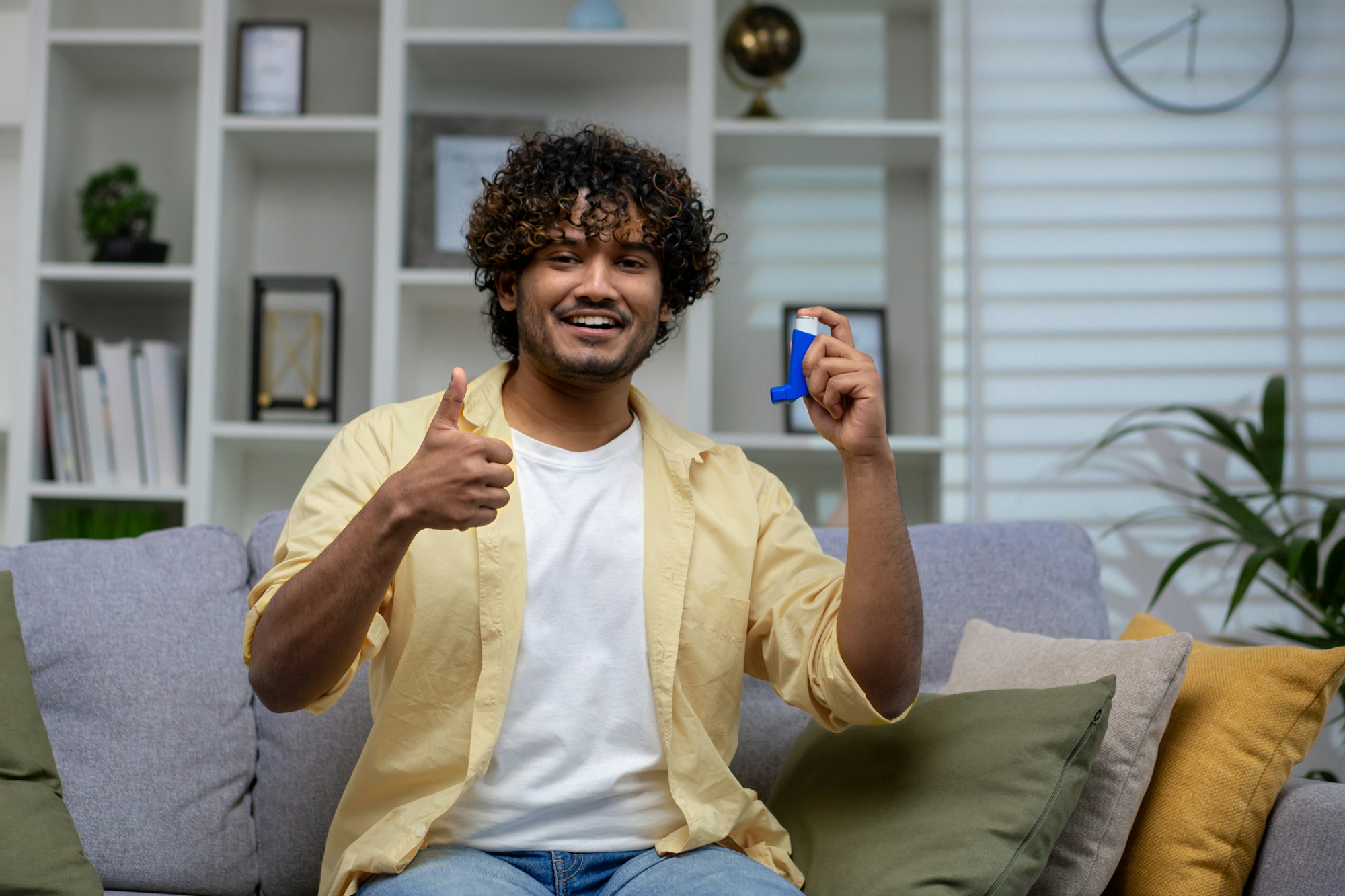 Man with asthma using an inhaler sitting on a sofa