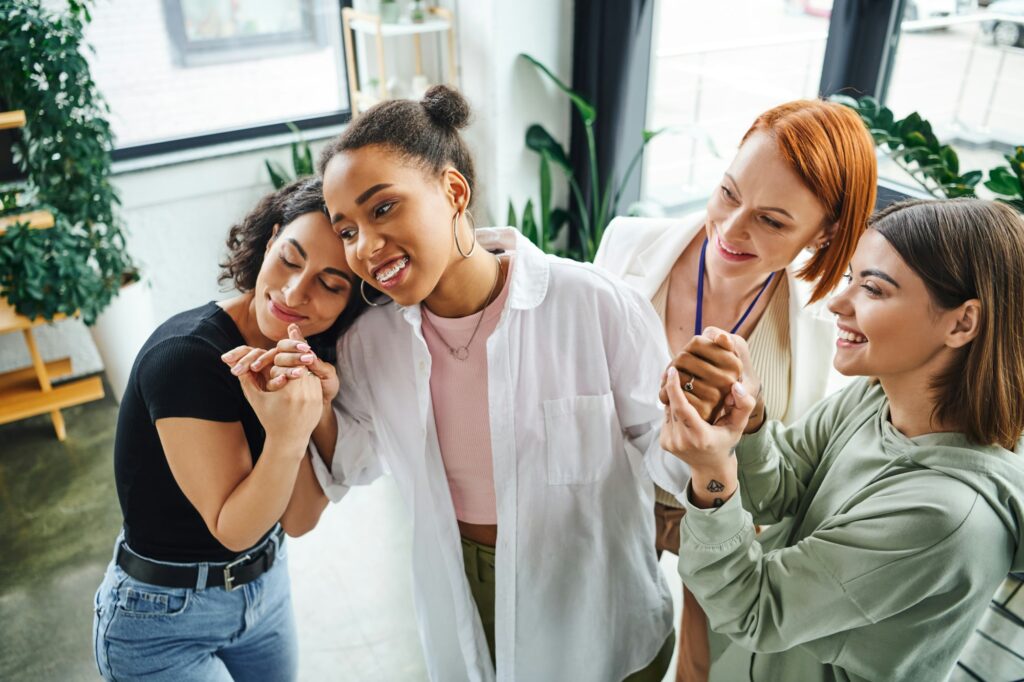 smiling multiethnic female friends and motivation coach holding hands of happy african american