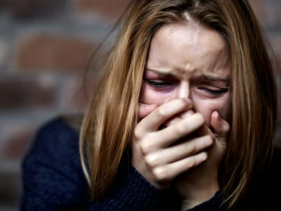 Emotionally victimized. Abused young woman crying hard and covering her mouth.