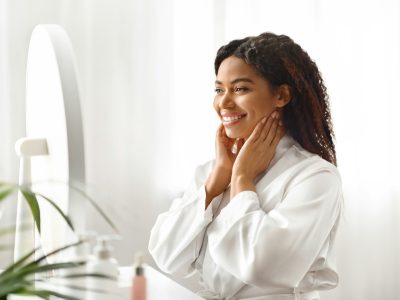 Self-Esteem. Attractive Black Woman Looking In Mirror At Home And Touching Face